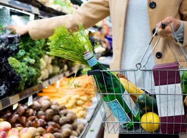 woman in white coat holding green shopping cart