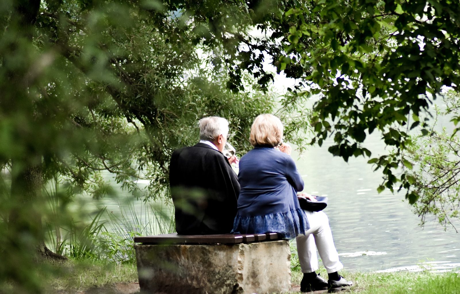 two people sitting on pavement facing on body of water