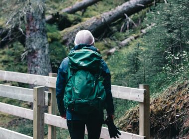 person in green and black jacket and black pants standing on brown wooden bridge during daytime
