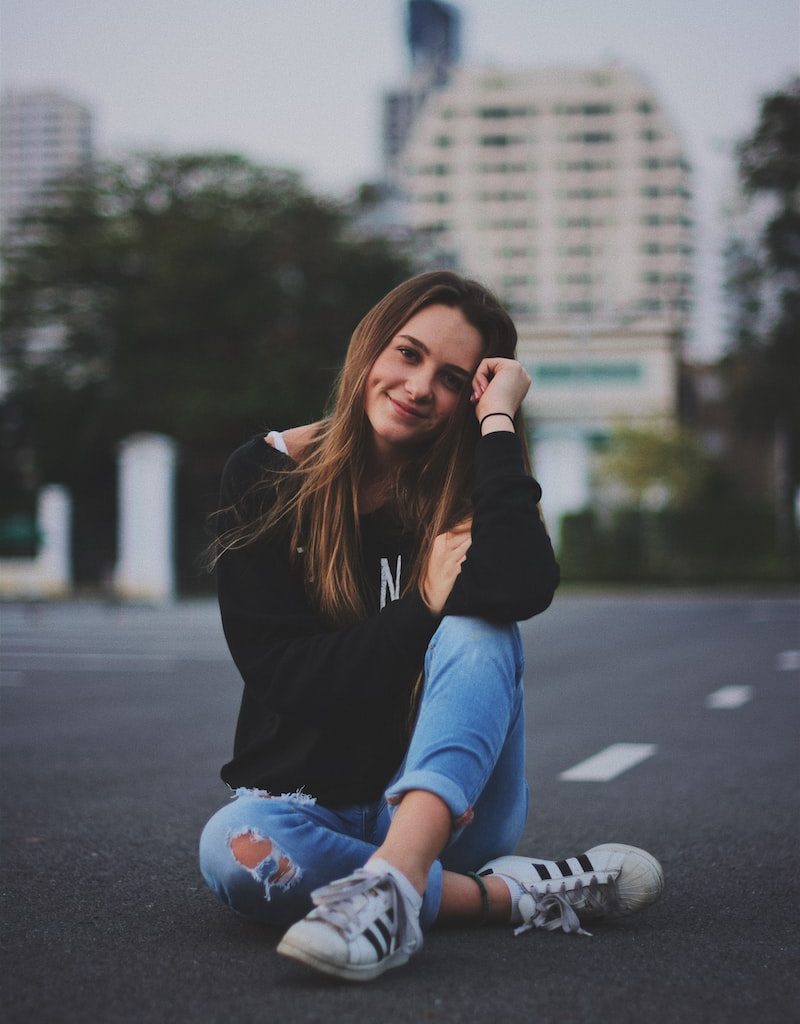 woman smiling while sitting on road with hand resting on top of her knee