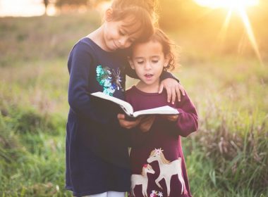 girl's left hand wrap around toddler while reading book during golden hour