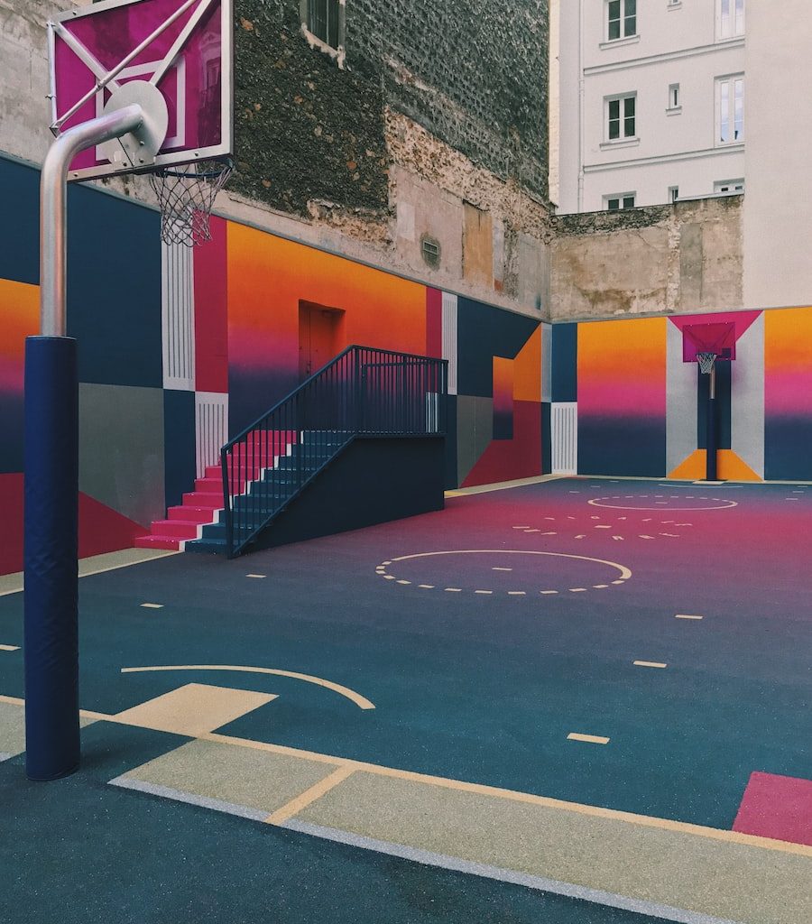 black, purple, and orange basketball court beside concrete buildings at daytime