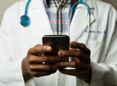 person wearing lavatory gown with green stethoscope on neck using phone while standing