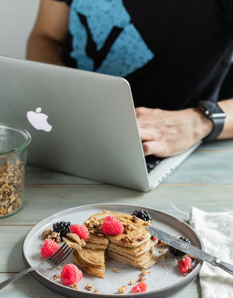 person holding silver macbook near cookies on white ceramic plate