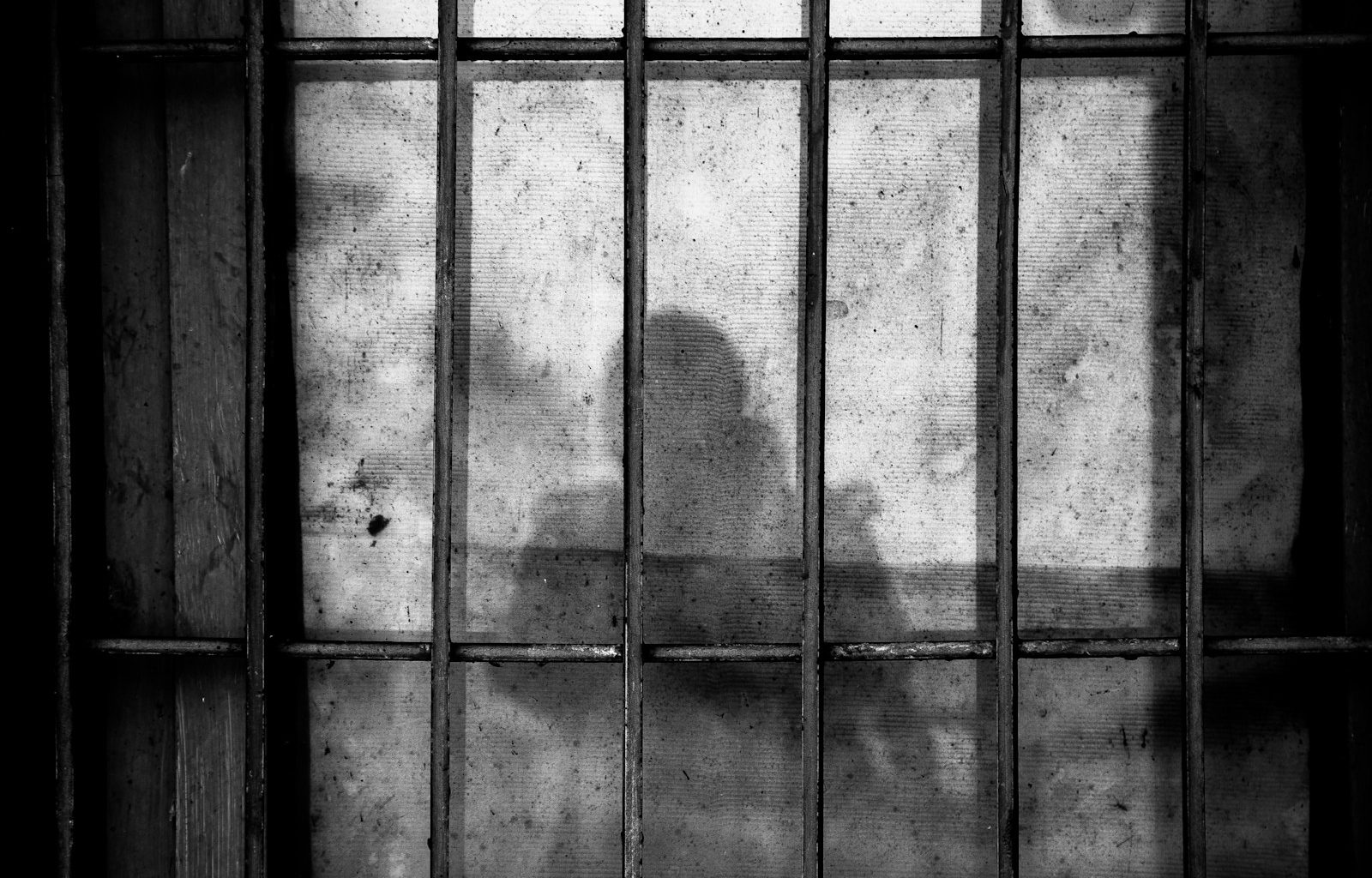 a shadow of a person behind bars in a jail cell