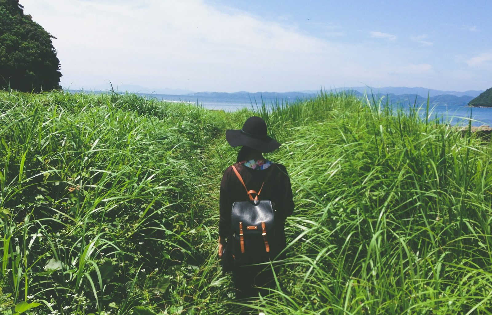 woman standing in the middle of green grass near sea at daytime