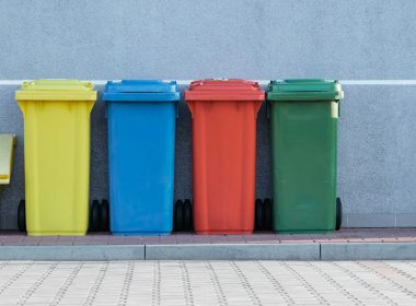 four assorted-color trash bins beside gray wall