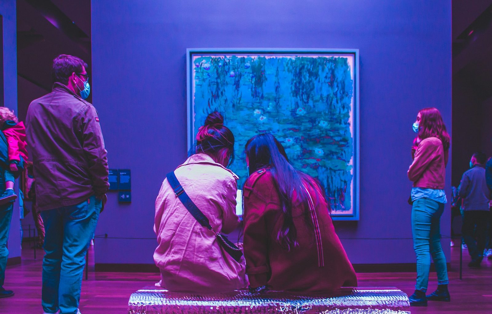two people sitting on a bench in front of a painting