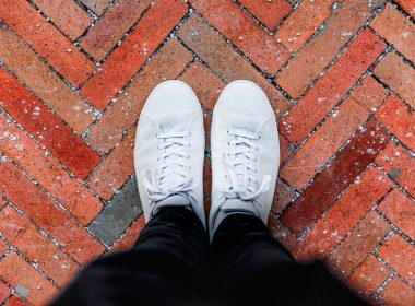 person wearing white sneakers standing on top of brown brick ground