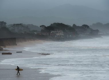 person walking and carrying surfboard on seashore during foggy weather