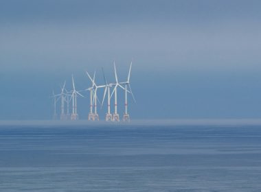 Offshore wind turbines stand in the misty ocean.