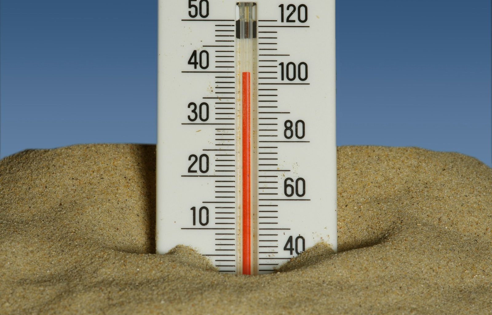 A thermometer in the sand with a blue sky in the background