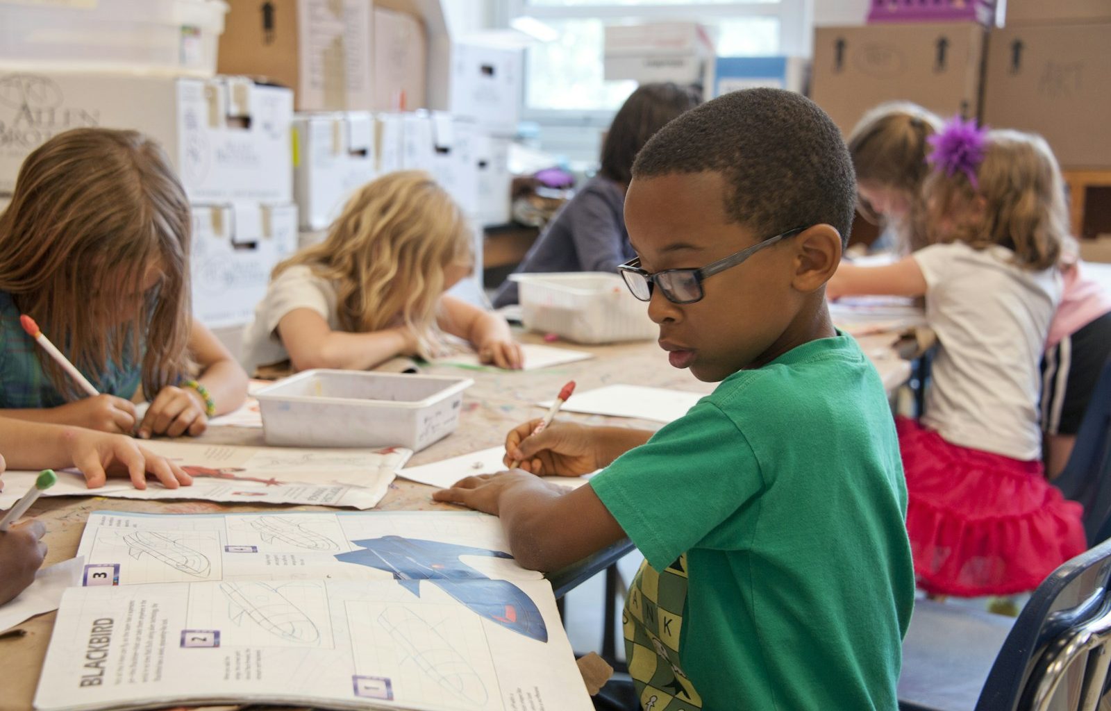 boy in green sweater writing on white paper