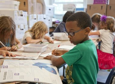 boy in green sweater writing on white paper