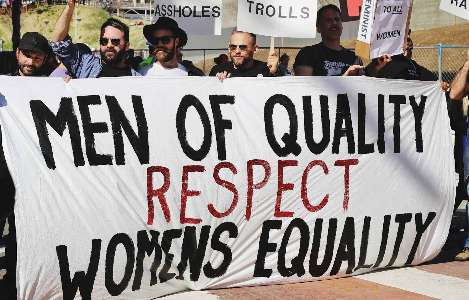 men holding white, black, and red Men of quality respect womens equality banner on road