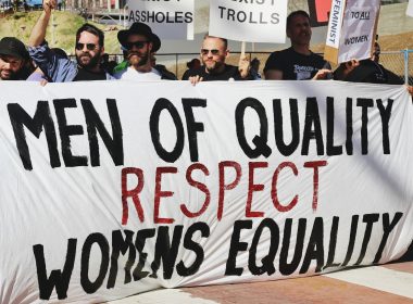 men holding white, black, and red Men of quality respect womens equality banner on road