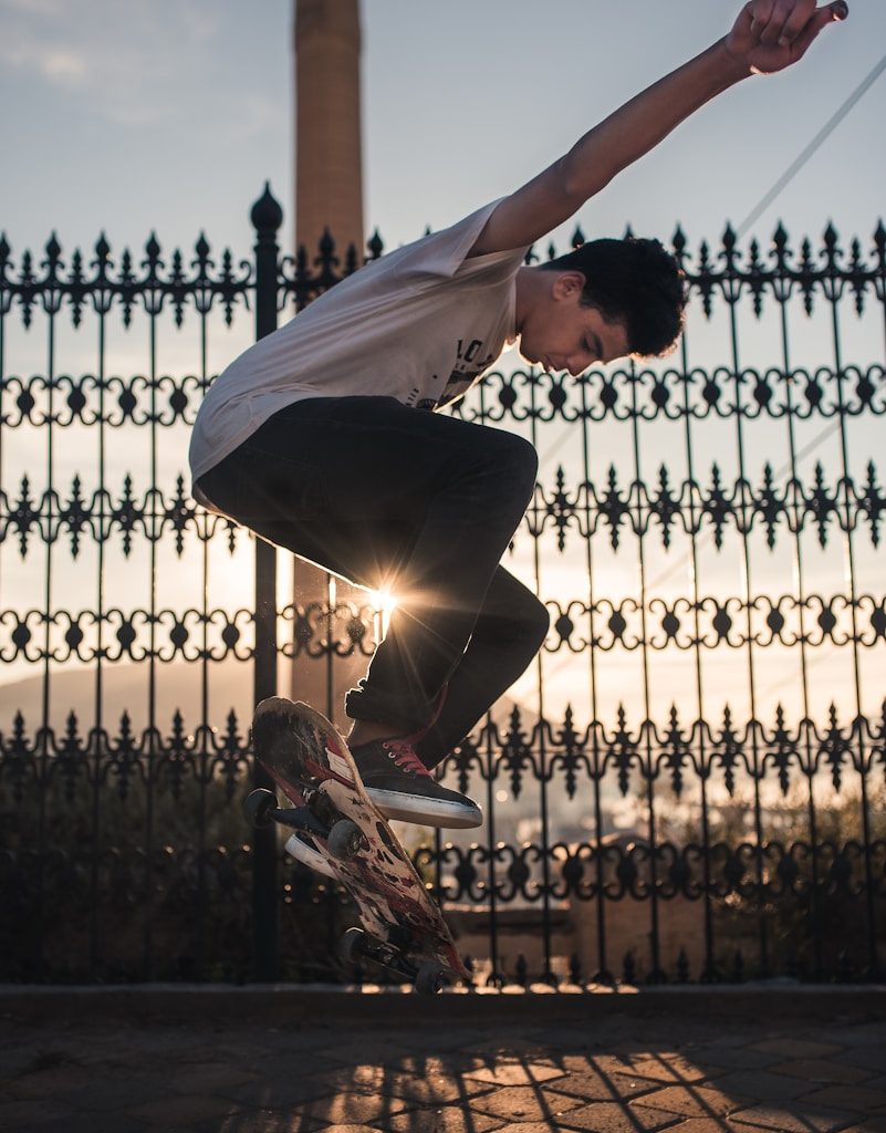 man doing skateboard trick near black steel fence during daytime