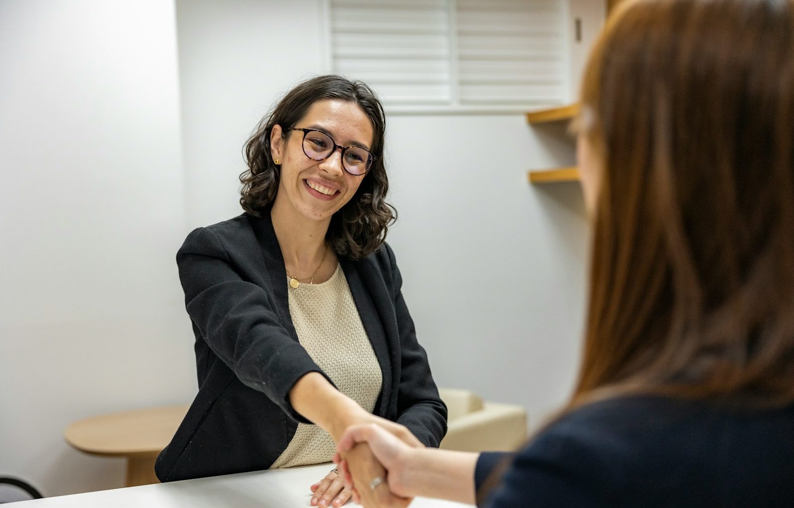a woman shaking hands with another woman sitting at a table