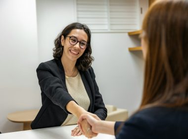 a woman shaking hands with another woman sitting at a table