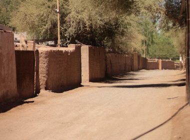 a dirt road with a building and trees in the background