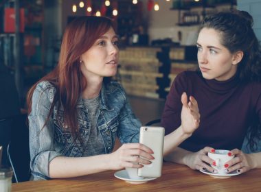 Two women converse at a cafe.