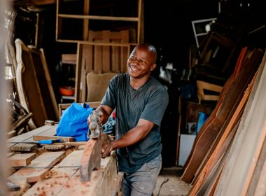 a man smiles as he works on a piece of wood