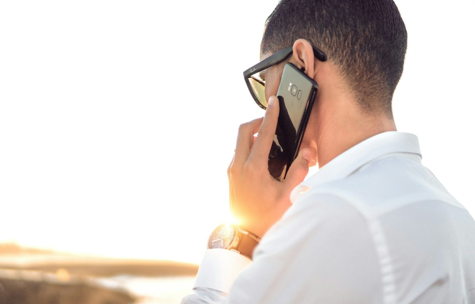 man holding smartphone standing in front of calm body of water
