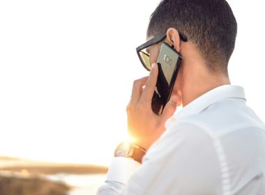 man holding smartphone standing in front of calm body of water