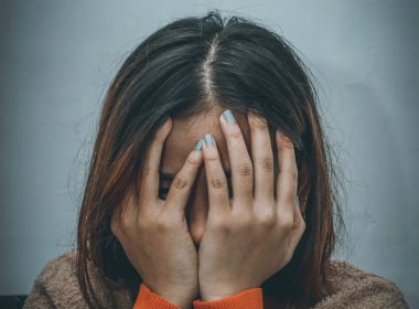 woman in brown sweater covering her face with her hand