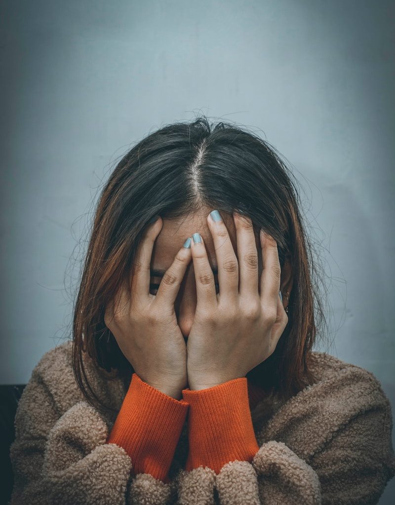 woman in brown sweater covering her face with her hand