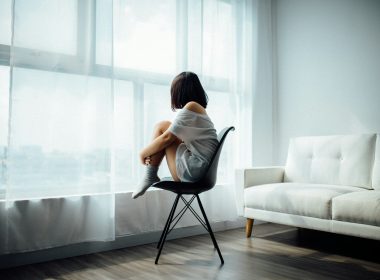 woman sitting on black chair in front of glass-panel window with white curtains