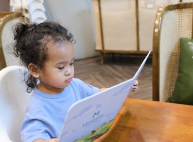 Young child sits in high chair reading a menu.