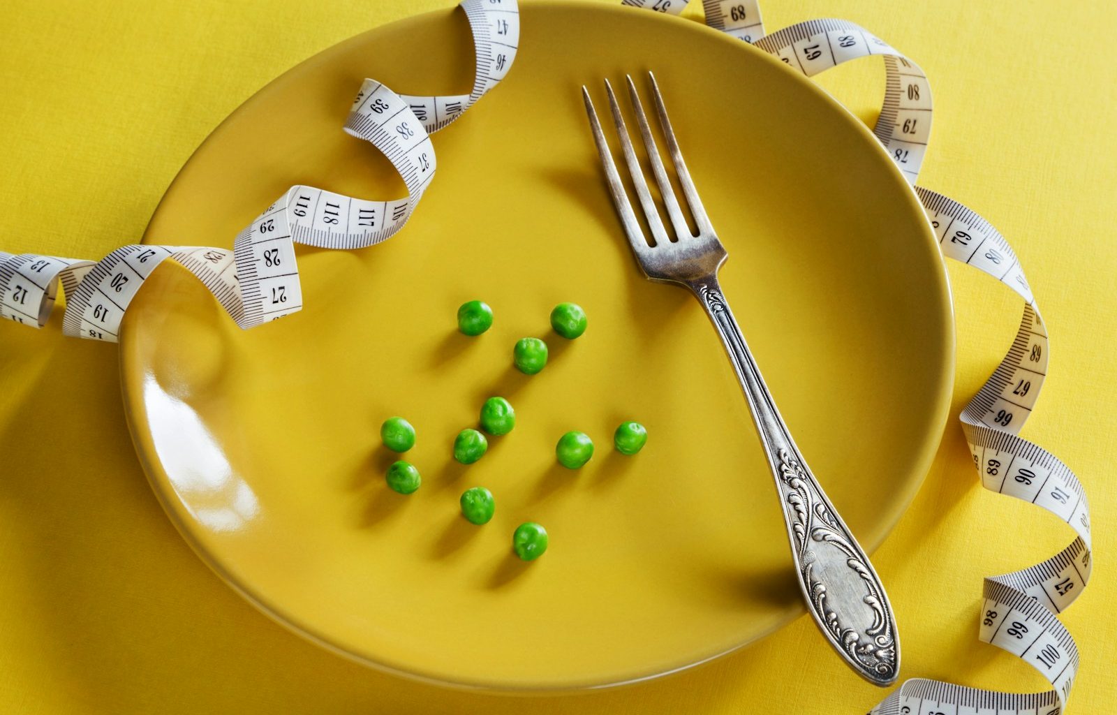 a plate with a fork, measuring tape and green peas