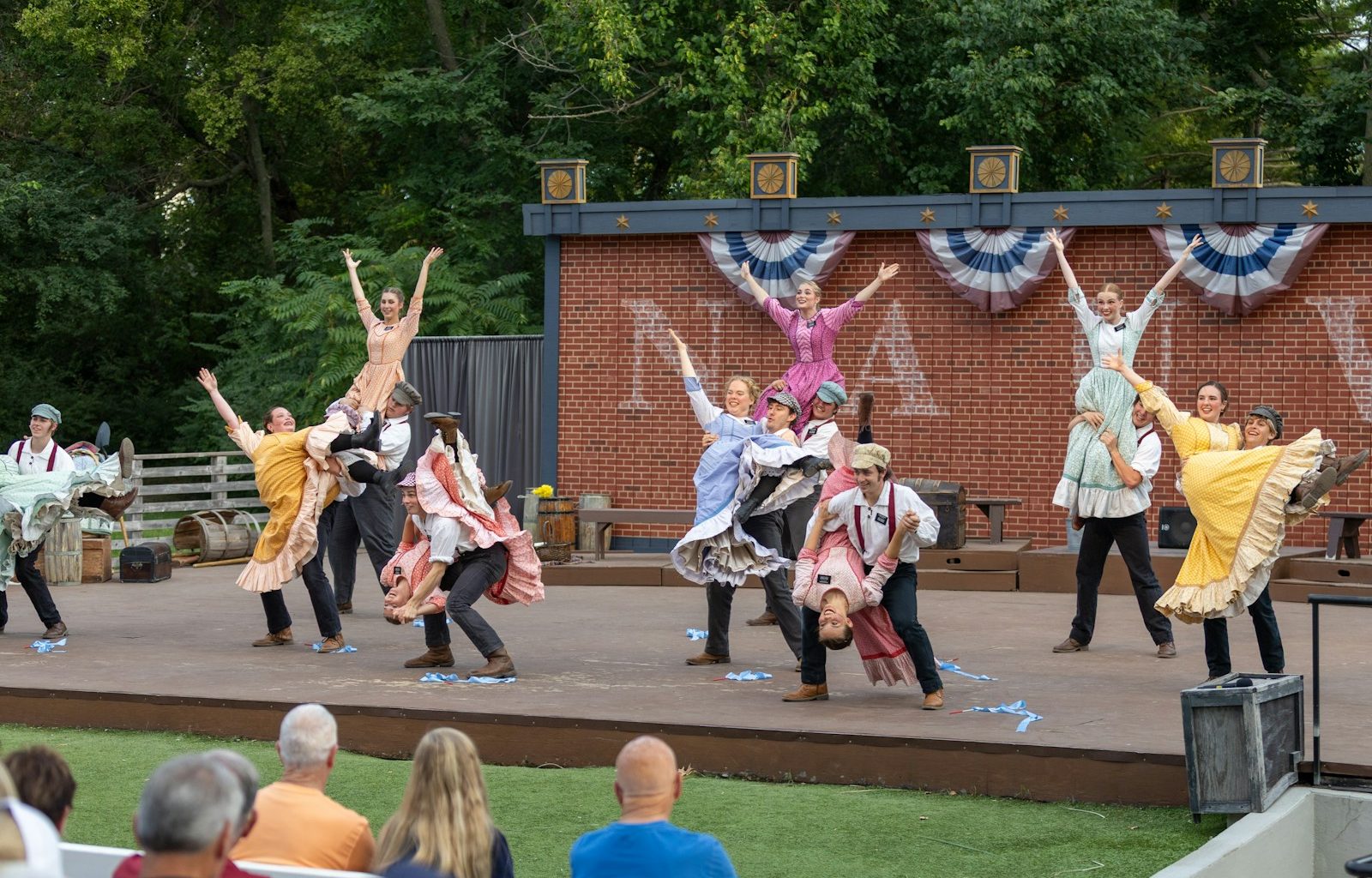 Performers dance on an outdoor stage with audience watching