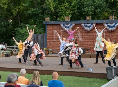 Performers dance on an outdoor stage with audience watching