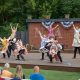 Performers dance on an outdoor stage with audience watching