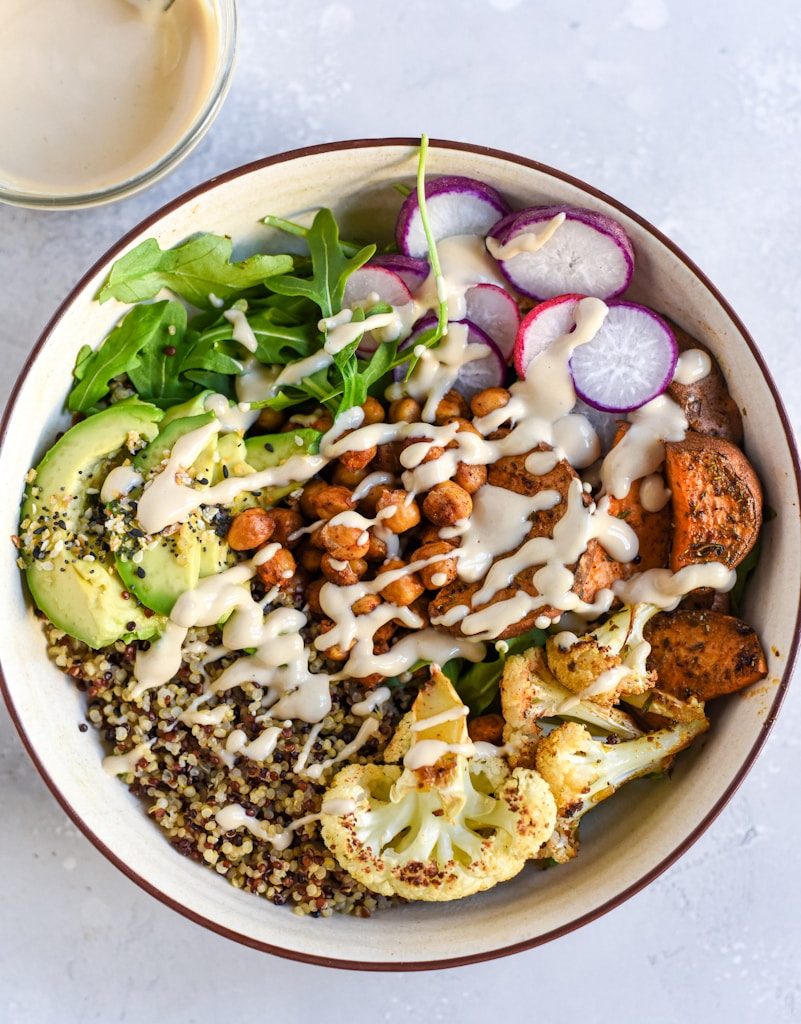 a bowl filled with vegetables and dressing next to a glass of milk