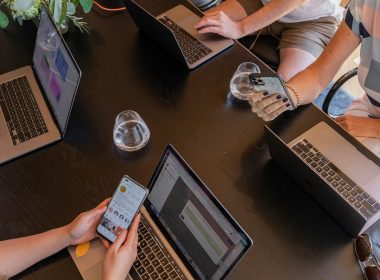 a group of people sitting around a table with laptops