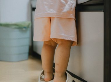 Toddler wearing oversized slippers stands by counter.