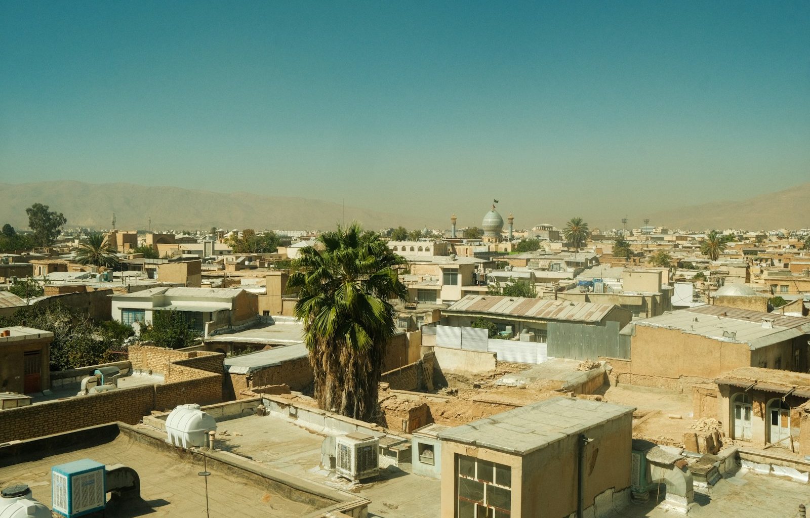 Overhead view of a dusty middle eastern city with palm trees.