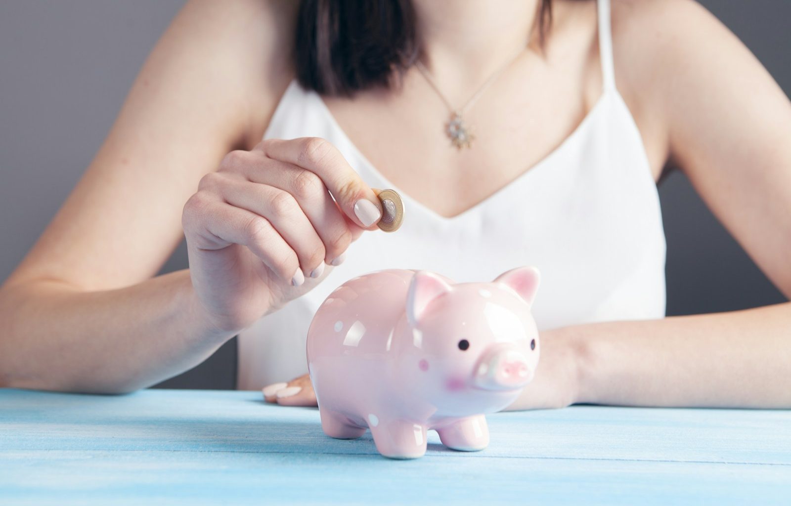 woman in white tank top holding pink pig figurine