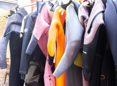A row of colorful wetsuits hanging on a rack outdoors