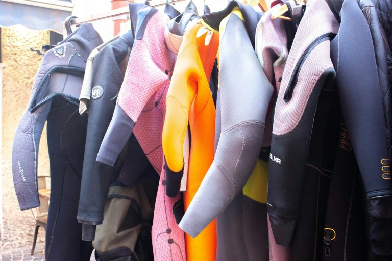 A row of colorful wetsuits hanging on a rack outdoors